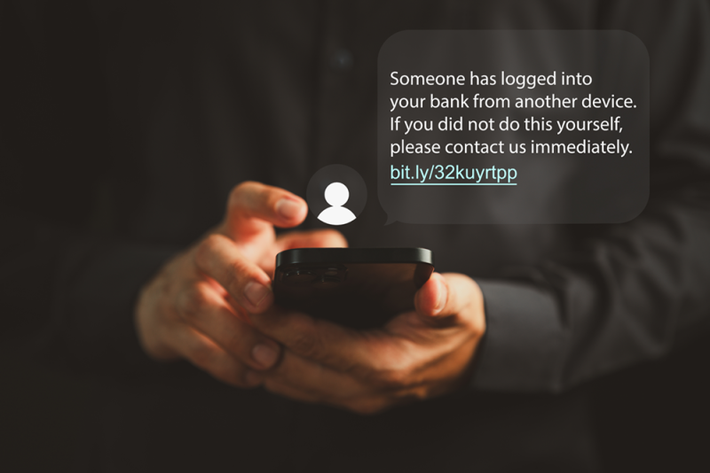 Cell phone in a person's hands with text that reads Someone has logged into your bank from another device. If you did not do this yourself, please contact us immediately. Fake url link provided.