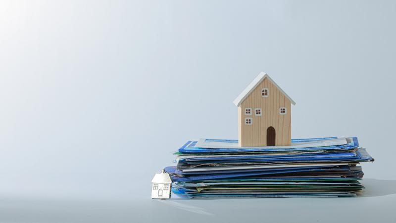 Miniature wooden house sitting on top of a pile of folders. 