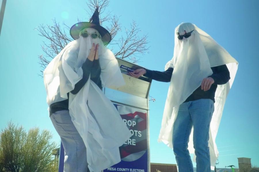 Two ghosts standing near a ballot box. 